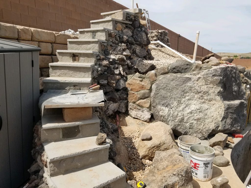Building a custom water feature in Saint George Utah using natural stone stairs leading up to a waterfall.